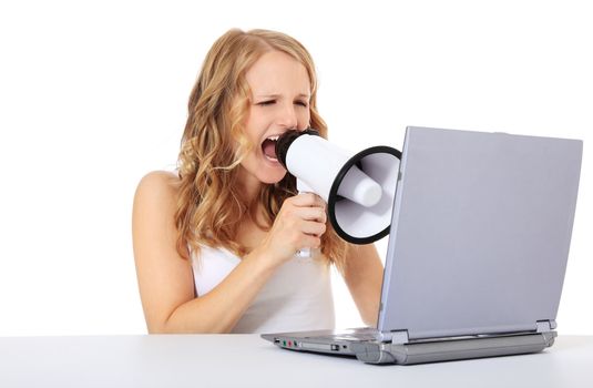 Attractive young woman uses megaphone while sitting in front of a computer / laptop. Isolated on white background.