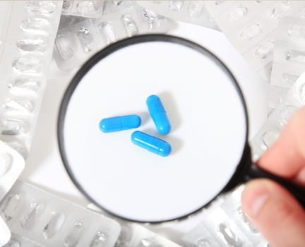 Conceptual shot of a person checking pharmaceuticals with magnifier. All on white background.