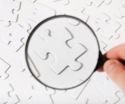 Conceptual shot of a person using a magnifier to check piece of a puzzle