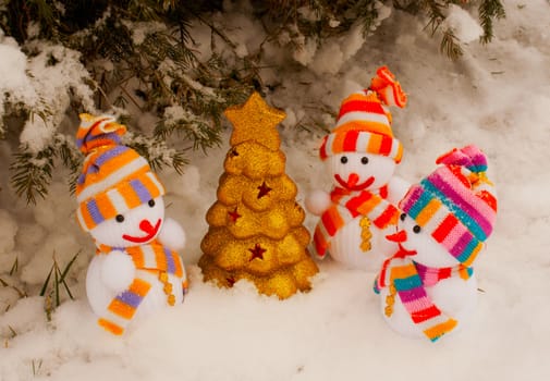 Three snowmen with golden evergreen tree staying outdoors