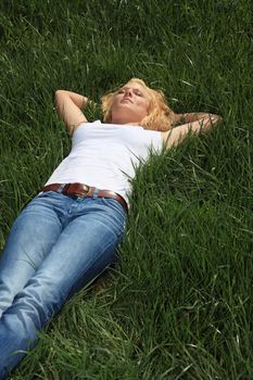 Attractive young woman resting outside on green meadow.