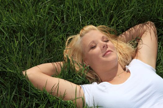 Attractive young woman resting outside on green meadow.