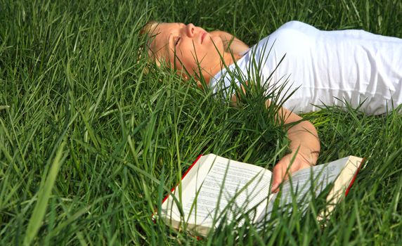 Attractive young woman resting outside on green meadow.