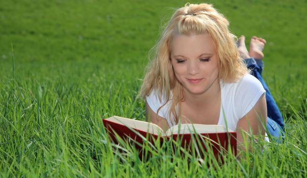 Attractive young woman resting outside on green meadow, reading a book.