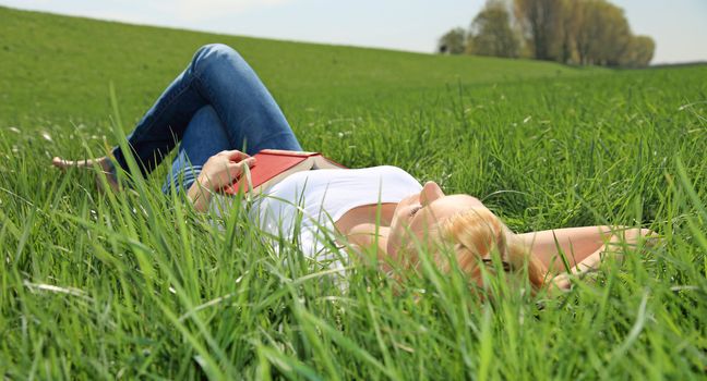 Attractive young woman resting outside on green meadow.