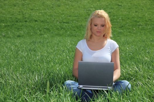 Attractive young woman resting outside on green meadow using laptop.