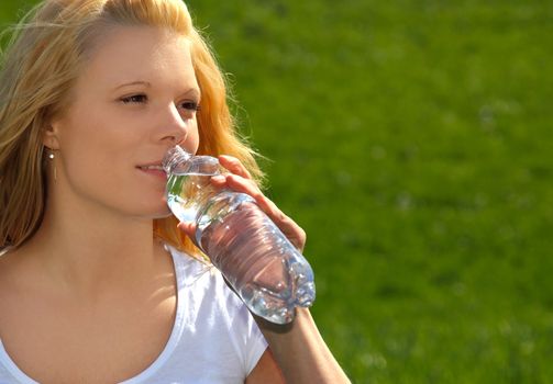 Attractive young woman resting outside on green meadow having a drink.