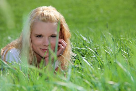 Attractive young woman resting outside on green meadow.