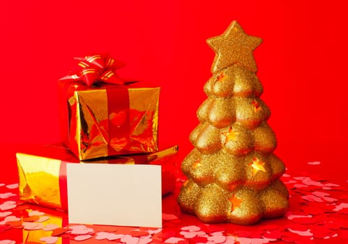 Two presents, blank card and golden evergreen tree over red background