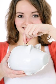 Attractive brunette girl puts money in her piggy bank. All on white background.