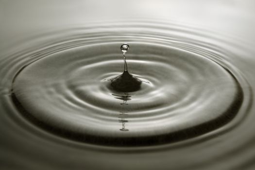Water droplet and concentric ripples on a grey surface.