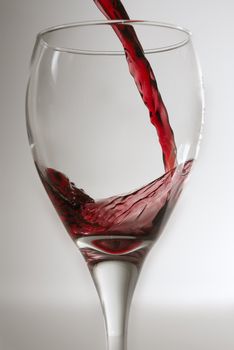 Red wine being poured into a clean wine glass against a grey backround.