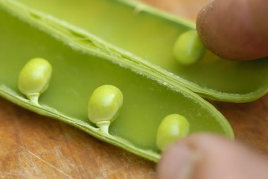 Peas (Pisum sativum) in a pod arranged on a wooden chopping board.