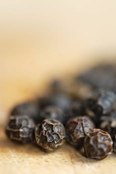 Macro image of pepper corns on a wooden chopping board.