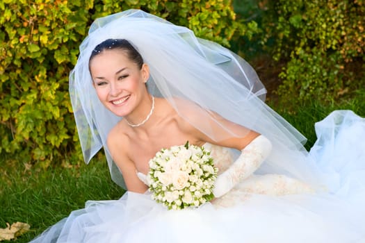 a portrait of the beautiful happy bride under the veil with a flower bouquet in her hands