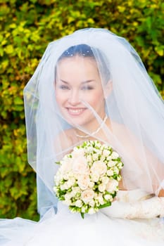 a portrait of the beautiful happy bride under the veil with a a flower bouquet in her hands