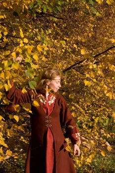 The blonde girl in medieval red dress in the autumn forest
