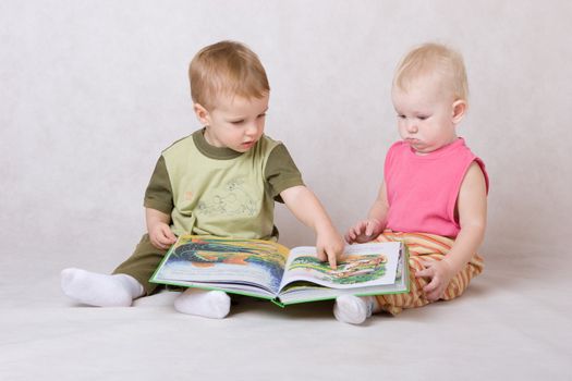 boy and the girl sit on a floor and read the book
