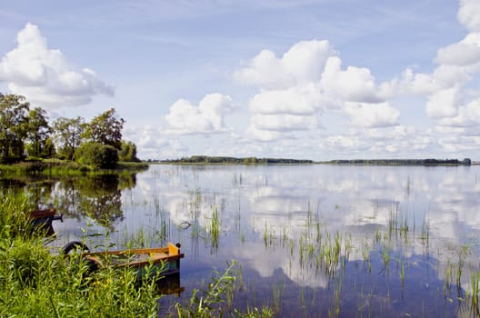 Amazing summer lake landscape, Boats on coast, clouds in sky and reflections on water.