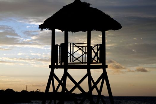 Tropical watchtower overlooking a beach silhouette at sunset