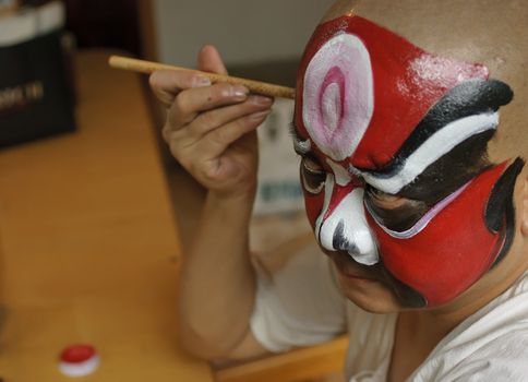 a chinese opera actor is painting his face backstage