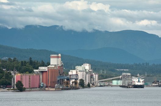 An ocean ship is loaded in the dock, with mountains and cloudy skies as backdrop.