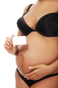 Belly closeup of a young beautiful pregnant woman holding a smal white chit in front of her tummy, over a white background.