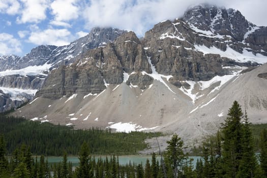 Blue cloudy skies top granite mountains over green forests and azure waters.