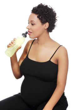 Site view of a young smiling pregnant woman taking a sip of an energy drink, isolated on a white background.