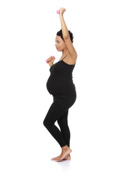 Full lenght site view of a young smiling pregnant woman doing exercises with small weights, isolated on a white background.