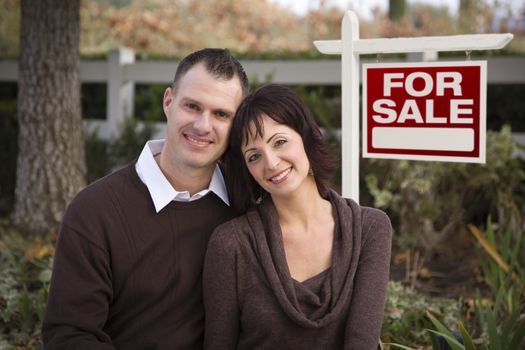 Happy Attractive Caucasian Couple in Front of Real Estate Sign.