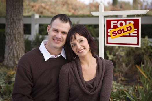 Happy Attractive Caucasian Couple in Front of Sold Real Estate Sign.