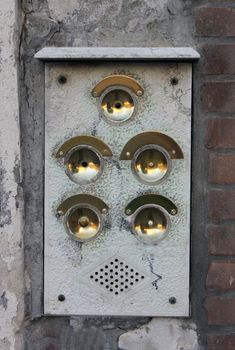 Five brass doorbells on a brick wall.