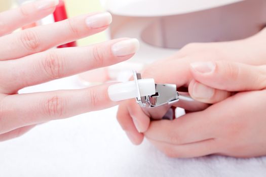 Manicurist trimming nail extensions on clients fingers 