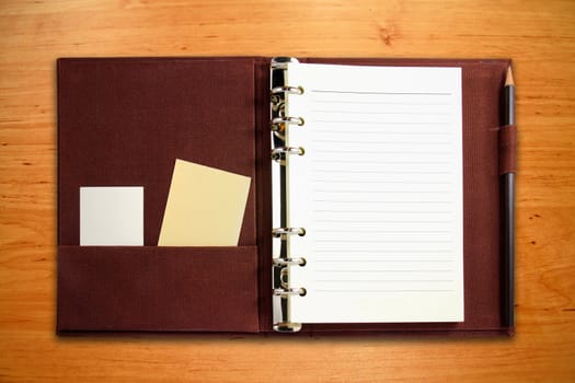 Brown canvas binder notebook with blank card and pencil on wooden background