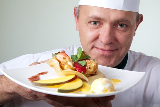 Close-up of chef holding plate with fruit dessert with ice cream, looking at camera