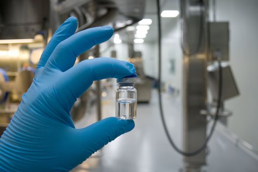 Hand in rubber glove holding a bottle of medicine against the background of the production line drugs