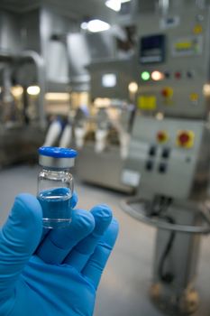 Hand in rubber glove holding a bottle of medicine against the background of the production line drugs