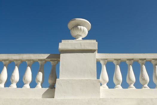 Old concrete park fence covered with white lime against the background of a blue sky