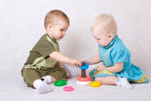 a boy and a girl of one and a half years old play pyramid sitting on the floor