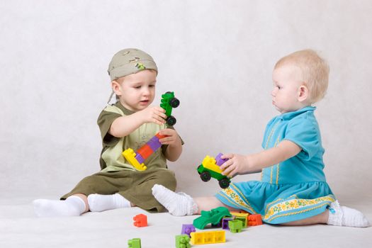 a boy and a girl of one and a half years old play the designer cubes on the floor
