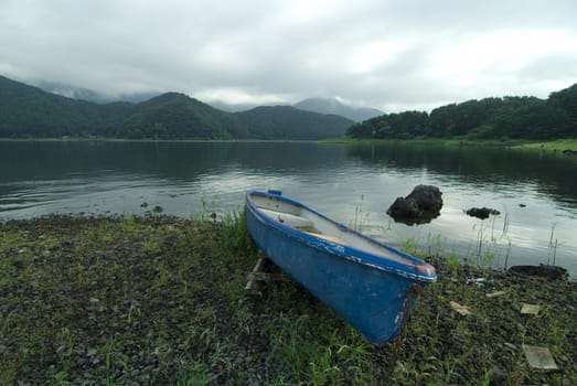 blue boat on the scenic mountain lake's shore at wet summer cloudy  weather