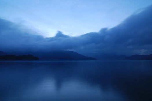 blue twilight photo of mountain lake in Japan with moving clouds and still water, Nikko, Japan