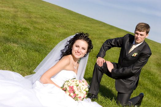 bride and groom sit on a green grass