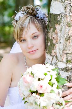 a bride with a flower bouquet embraces a tree