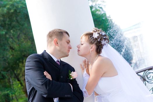 a bride and a groom stand by a white column and kiss