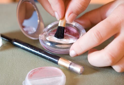 Brush for a make-up in hands at the visagiste, a shadow and a pencil