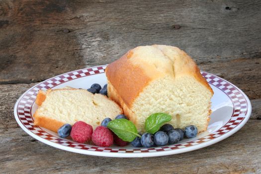 Pound cake loaf with a couple of slices and fresh raspberries and blueberries.  Garnished with mint leaves.
