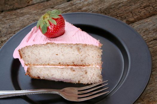 Strawberry cake with strawberry icing and garnished with a fresh strawberry.