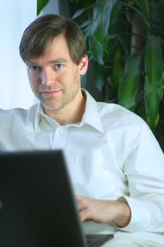 Handsome businessman working on laptop in casual attire.